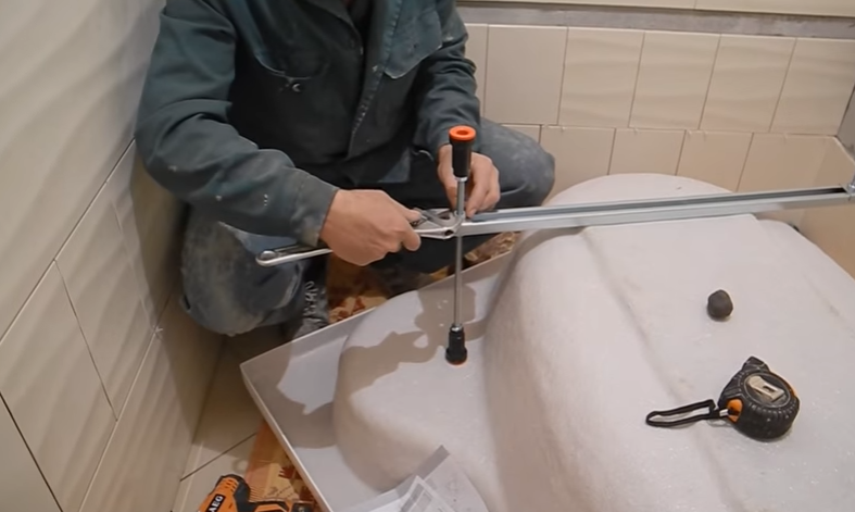 Мастер затягивает гайки на ножке ванны